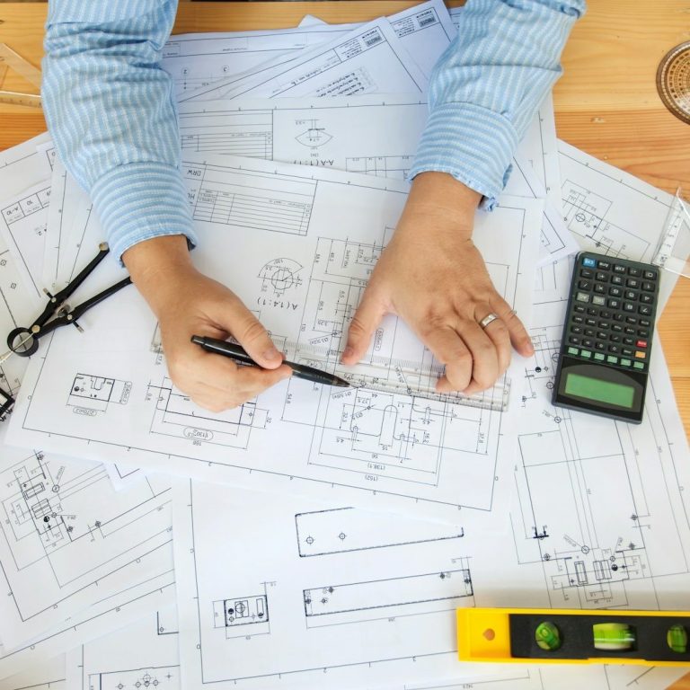 Hände skizzieren Pläne auf Bauzeichnungen, umgeben von Werkzeugen.