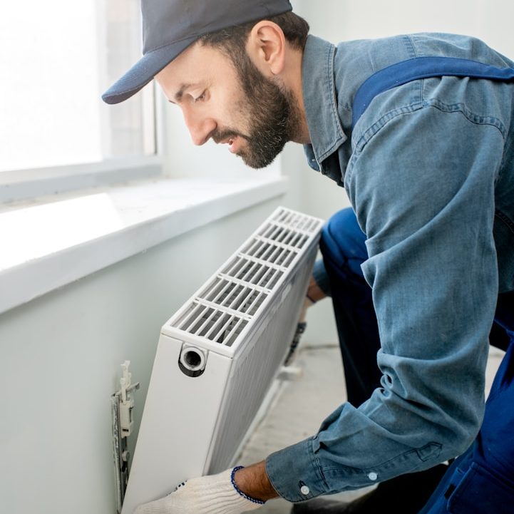 Handwerker installiert eine Heizung in einem hellen Raum neben einem Fenster.